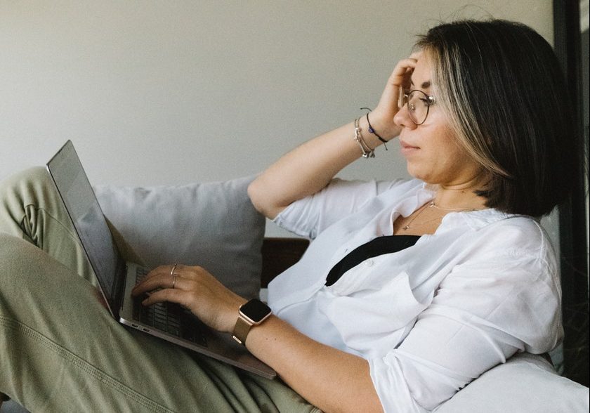 Focused female freelancer working distantly on laptop sitting on couch
